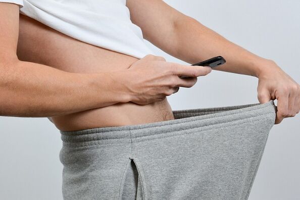 egy férfi lenéz a nadrágján egy megnagyobbodott péniszre